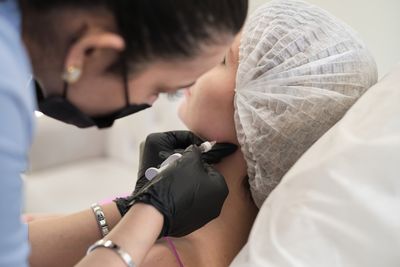 Doctor injecting a syringe of liquid into a woman's jawline in a hospital