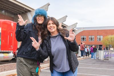 NAU students smile and do the Lumberjack hand symbol on a snowwy day in Flagstaff.